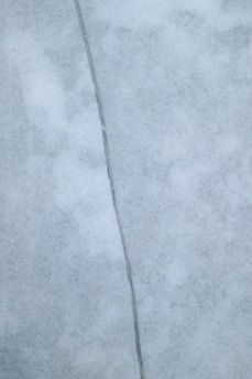 A close-up view of a surface with a noticeable crack running vertically through the center. The surface appears to be made of a smooth, marble-like material with a light gray color and subtle texture variations.