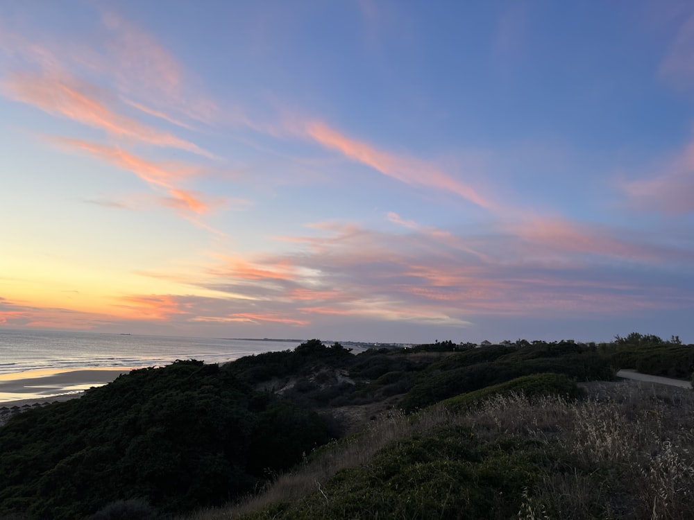 a sunset view of a beach with a hill in the foreground