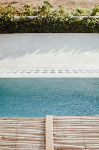 A bright, inviting swimming pool surrounded by lush greenery and Acqua branded pool products neatly arranged nearby.