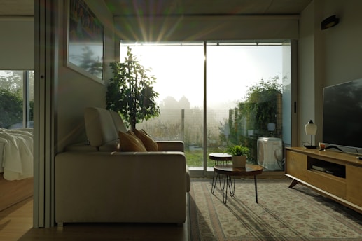 A serene, sunlit living room featuring a beige sofa adorned with soft earth-toned pillows and a minimalist coffee table with a vase of fresh greenery.