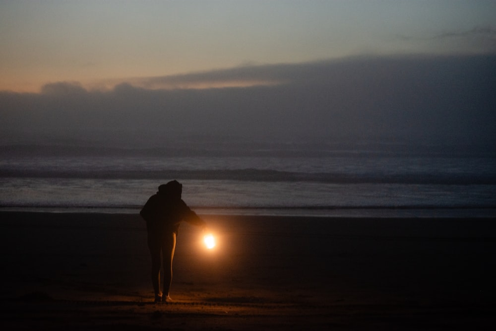 una persona parada en una playa con una linterna en la mano