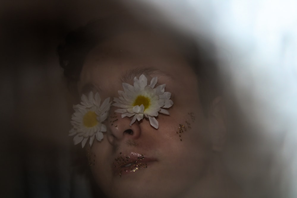 a woman with flowers on her face looking through a mirror