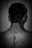 A black and white image depicting the back of a person. The focus is on the spine area, which appears to have a long scar adorned with small flowers. The lighting creates a soft contrast against the skin.