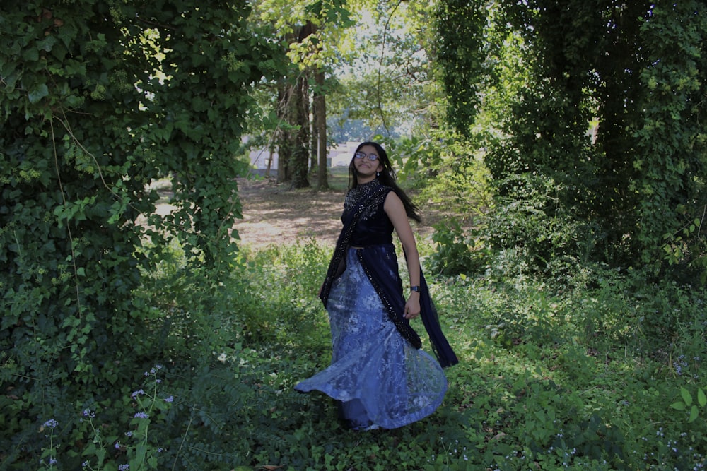 a woman in a blue dress walking through a forest