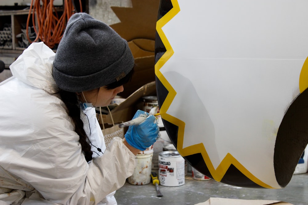 a woman in a white coat painting a large object