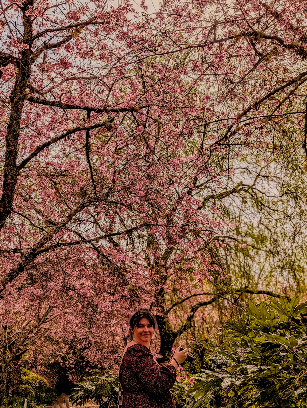 una mujer de pie frente a un árbol con flores rosadas