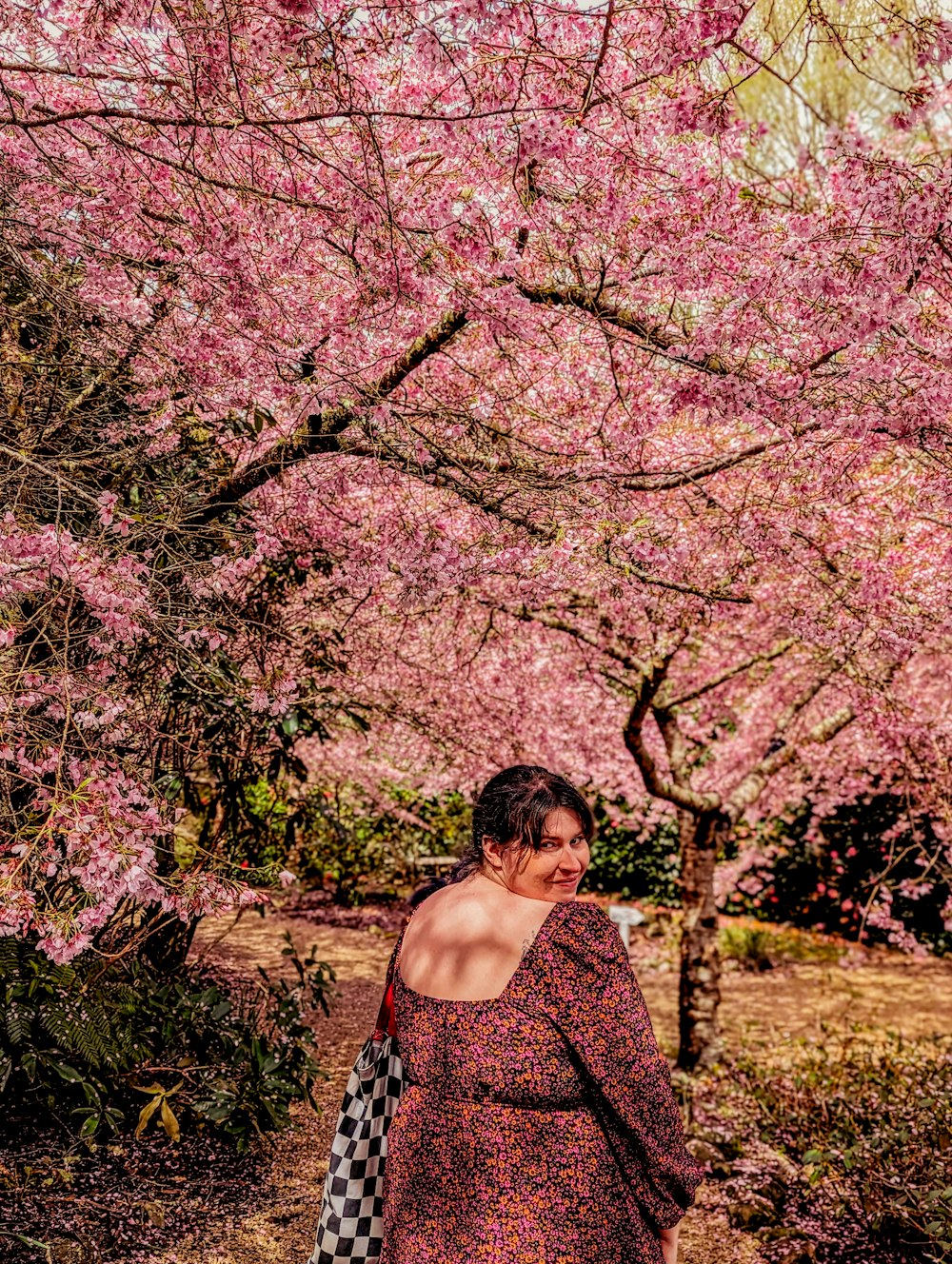 a woman in a dress is walking under a tree with pink flowers