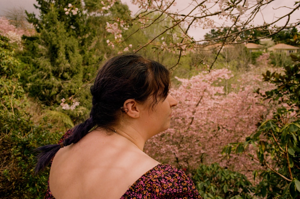 a woman standing in front of a tree filled with pink flowers