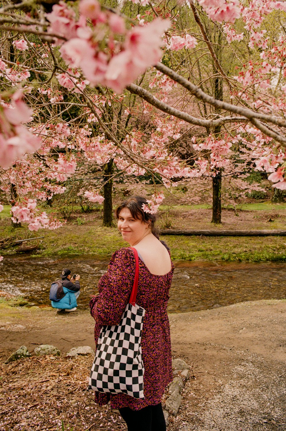 una mujer de pie bajo un árbol con flores rosadas