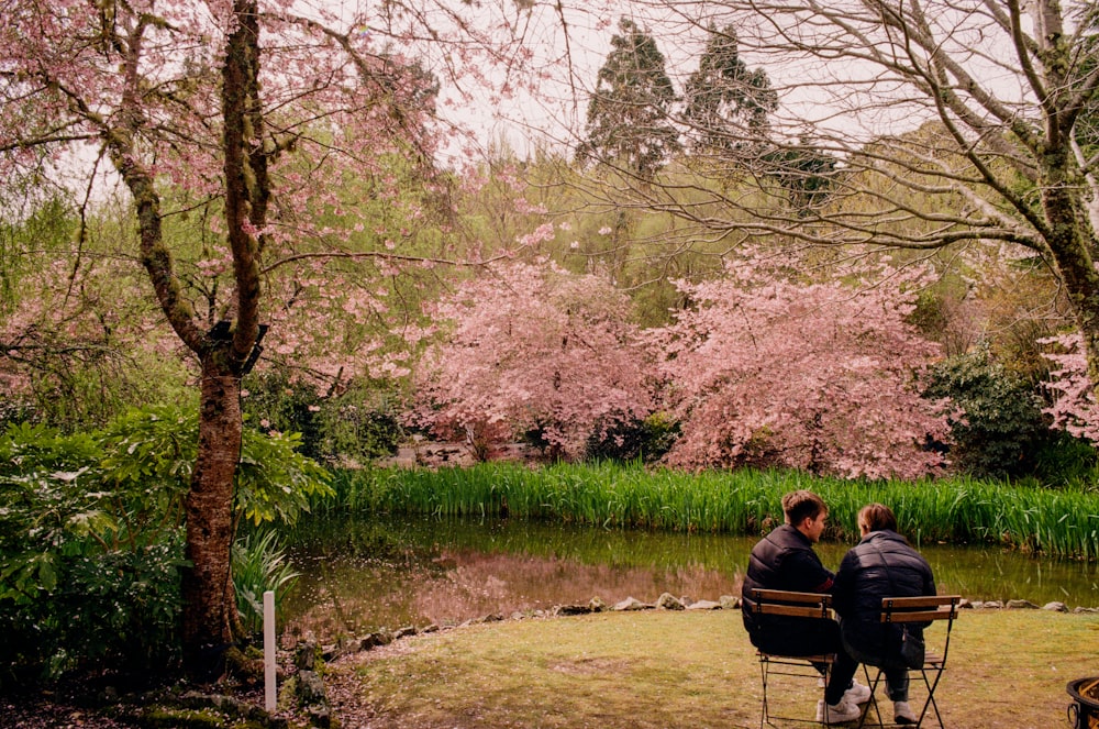 zwei Personen sitzen auf einer Bank in der Nähe eines Teiches
