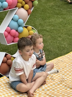 Two children laughing together while drawing with crayons on a picnic blanket.