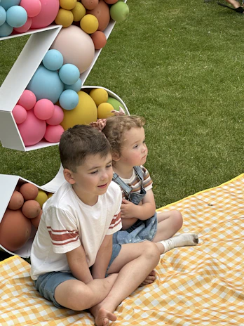 A group of children wearing comfortable casual outfits, sitting together on a bright picnic blanket.