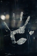A blurred handprint, possibly on glass or a reflective surface, with smudges and fingerprints visible. The background is dark, enhancing the visibility of the handprint.