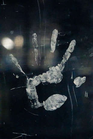 A blurred handprint, possibly on glass or a reflective surface, with smudges and fingerprints visible. The background is dark, enhancing the visibility of the handprint.