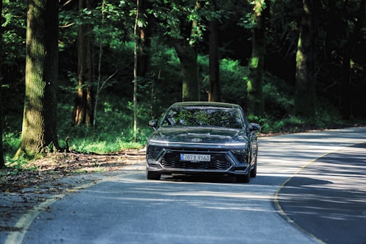 A sleek modern car driving on a winding road surrounded by lush greenery.
