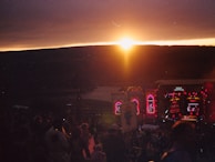 A sunset view over a bustling outdoor concert with people dancing and enjoying live music.