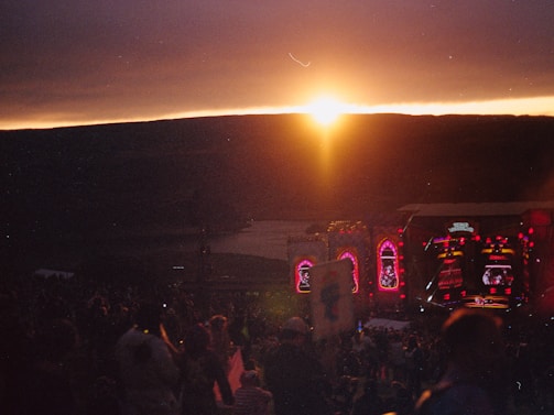 A sunset view over a festival stage, filled with lights.