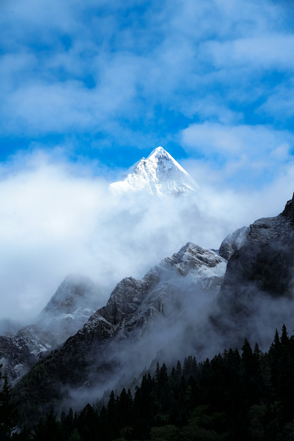 a mountain covered in clouds and trees under a blue sky