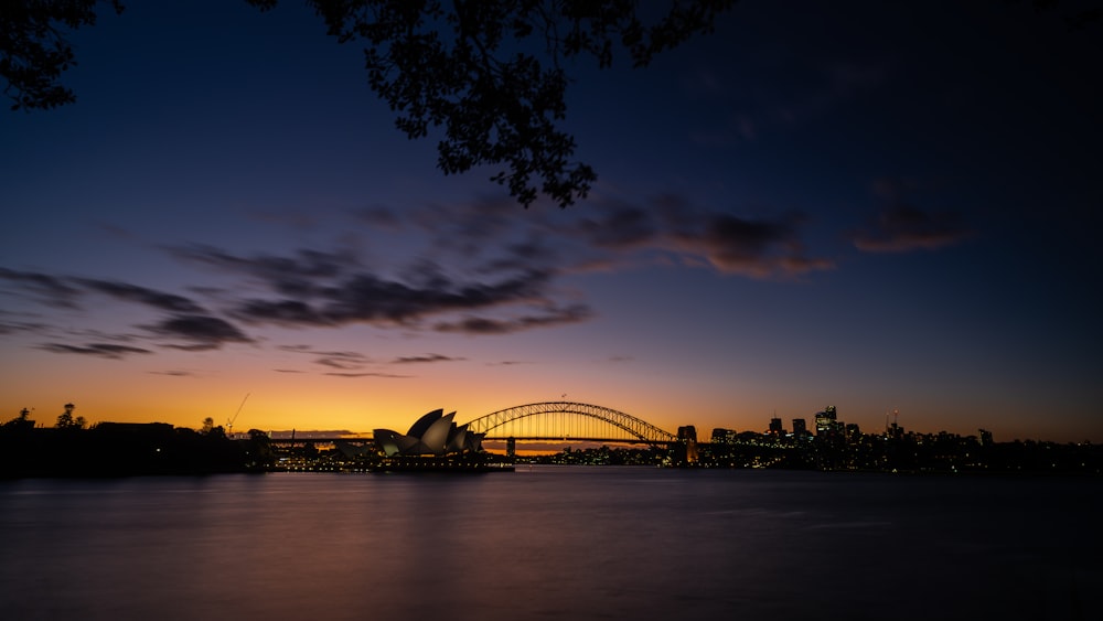 the sun is setting over the water with a bridge in the background