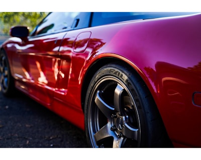 Red compact car angled to highlight its sporty design and shiny rims.