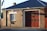 A brick building with a large garage door and a sign reading 'Fire + Rescue'. The structure has a dark sloped roof, a window with white panes, and an Australian flag visible in the background. The sunlight casts shadows on the brick wall.