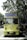 A vintage-style yellow bus with 'Bandung Tour on Bus' written on the front, parked on a tree-lined street. The bus has round headlights and a distinctive front design. Several people are standing nearby, some wearing masks. The surrounding environment is lush with green trees, and there's a streetlamp with a globe light.