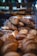 A variety of artisan breads are displayed in a bakery setting. The loaves have a rustic appearance with golden-brown crusts, some dusted with flour. They are arranged in a pyramid shape, creating a visually appealing display under soft lighting.