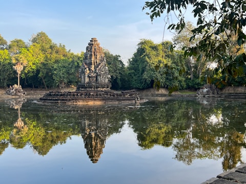 A serene temple in Bali surrounded by lush greenery and calm water reflecting the sky.