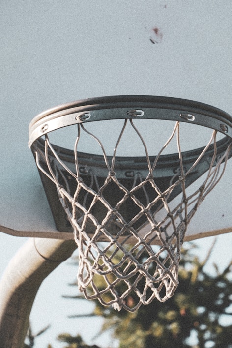 A close-up shot of a basketball hoop with a net swaying gently in the breeze at an outdoor court.