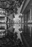 Black and white street scene capturing a lone figure reflected in a rain puddle on a quiet Indian alley.