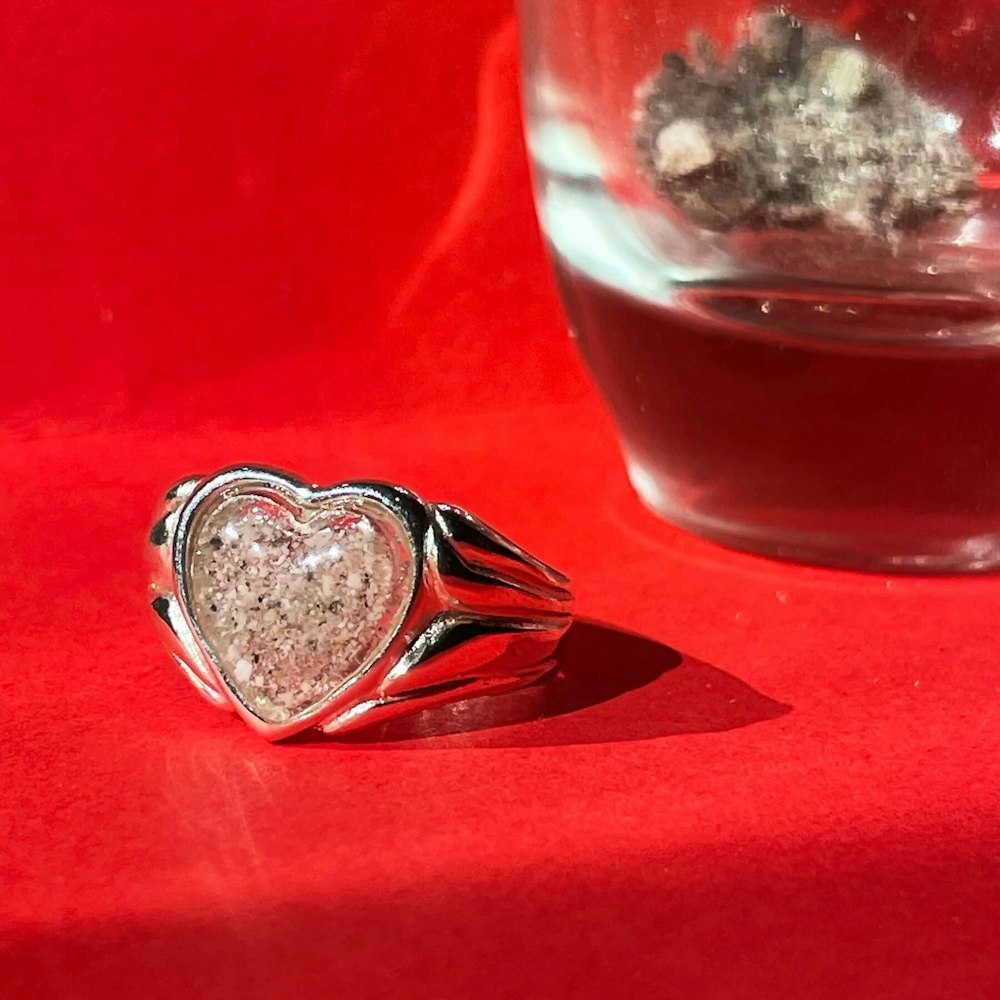 a heart shaped ring sitting next to a glass of water