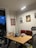 A cozy workspace, featuring a wooden desk with various decorative items such as picture frames, a vase, and candles. Above the desk, there are framed artworks on the wall. The space is softly illuminated by a stylish curved floor lamp. The atmosphere feels inviting and personal.
