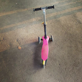 A foldable kick scooter with big wheels standing on a sunny park path.