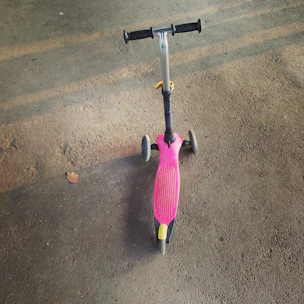 A foldable kick scooter with big wheels standing on a sunny park path.