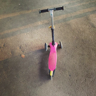 A foldable kick scooter with big PU wheels standing on a sunny park path.