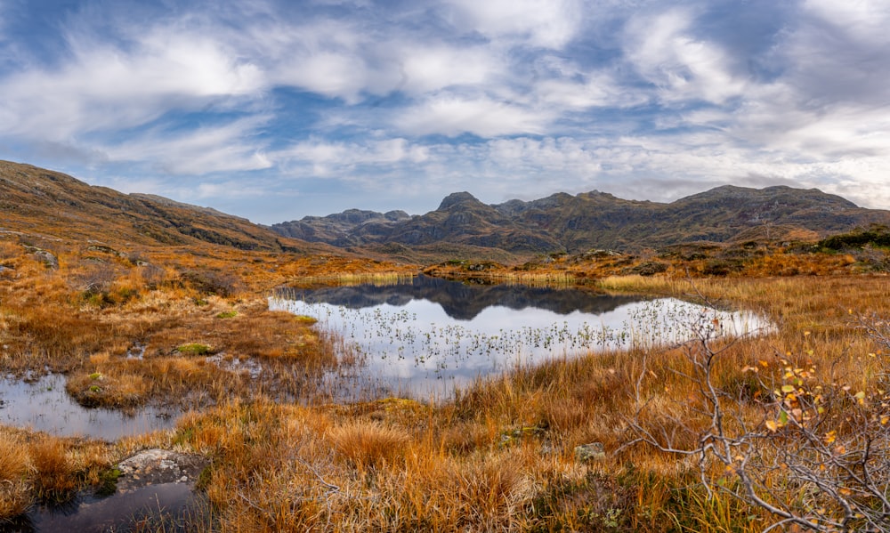 a small lake surrounded by mountains under a cloudy sky