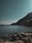 A serene coastal landscape with calm waters and distant mountains under a clear sky.
