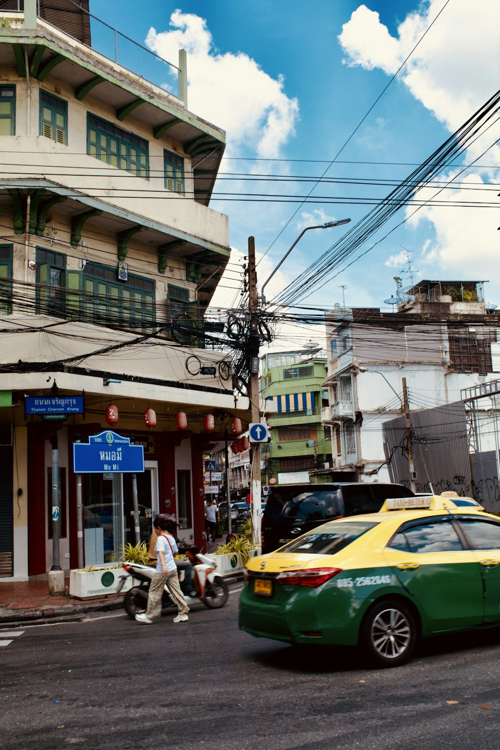 a yellow and green car driving down a street next to a tall building