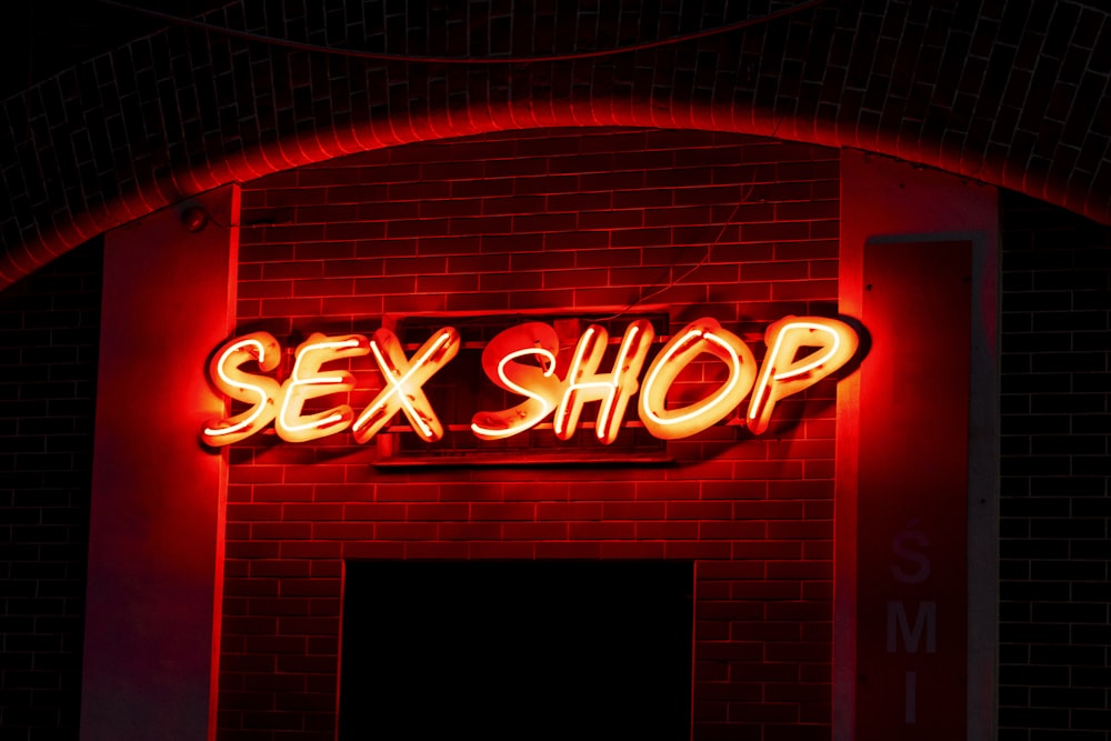 a neon sign that reads sex shop on a brick wall