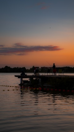 A serene lakeside scene with an instructor guiding a small group of anglers casting their lines at sunset.
