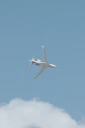 A sleek cargo airplane soaring above white clouds against a bright blue sky.