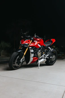 A sleek red motorcycle parked under city lights at night, highlighting its modern design.