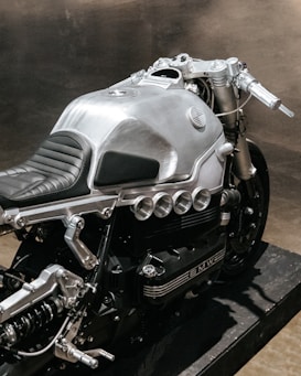 A sleek, silver motorcycle showcasing a modern, metallic design with visible components and a black cushioned seat. The motorcycle features intricate engineering details and a sturdy frame, emphasizing its mechanical aesthetic.