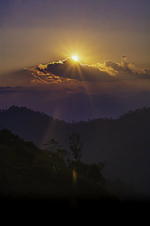 Golden sunset rays filtering through wispy clouds over a serene landscape in earthy tones.