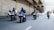 A group of motorcyclists riding together on a multi-lane road under an overpass. All riders are wearing helmets and protective gear. The scene appears to be urban with concrete structures and multiple lanes for traffic. Some cars can be seen in the background.