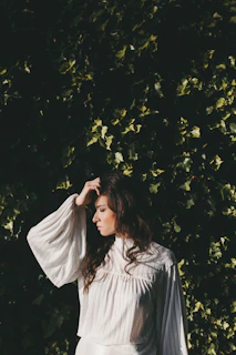 A serene woman wearing a flowing ivory blouse from the Quietly Powerful collection, standing against a soft terracotta wall.