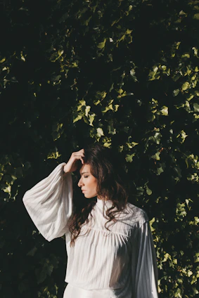 A serene woman wearing a flowing ivory blouse from the Quietly Powerful collection, standing against a soft terracotta wall.