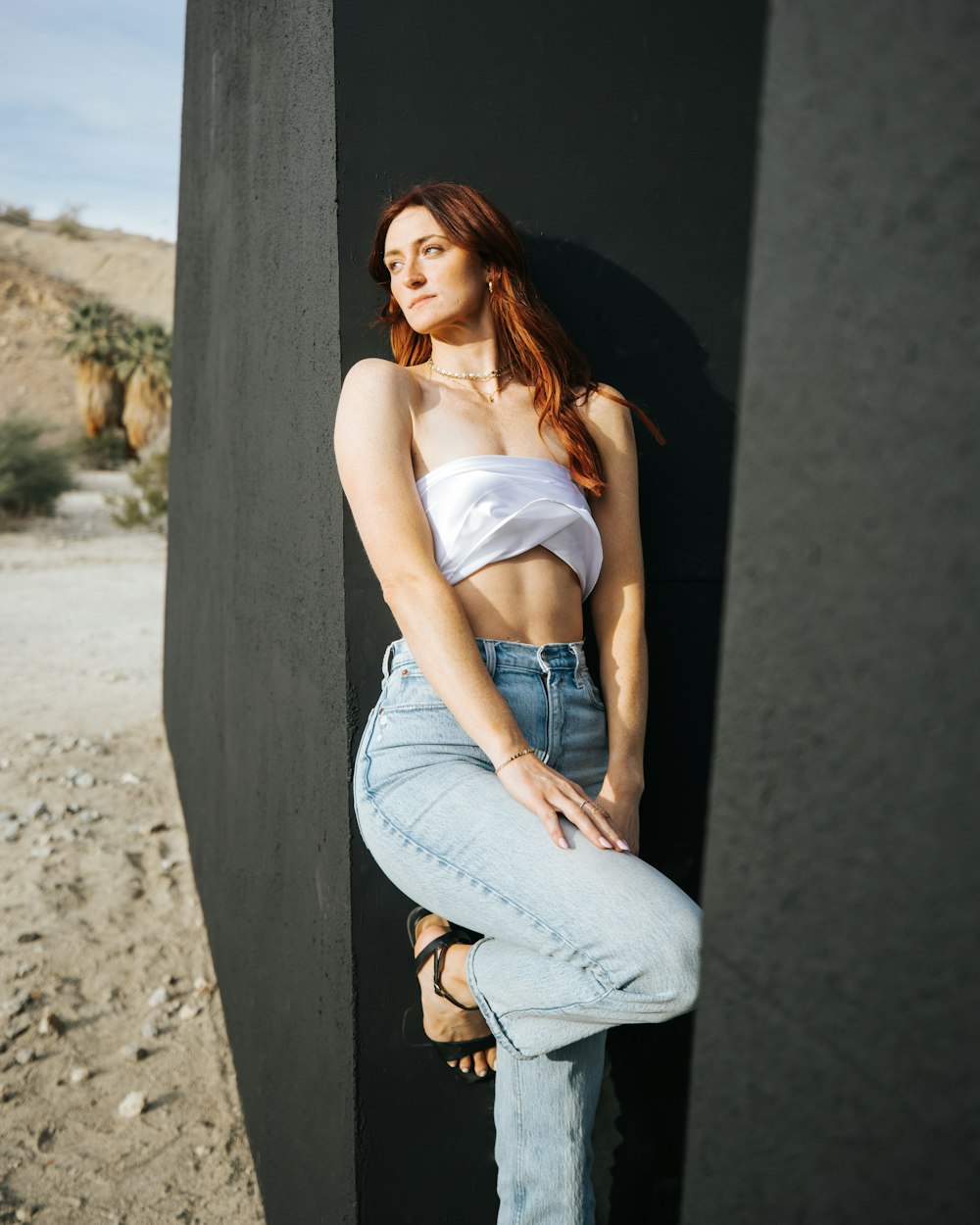 a woman leaning against a wall with her legs crossed