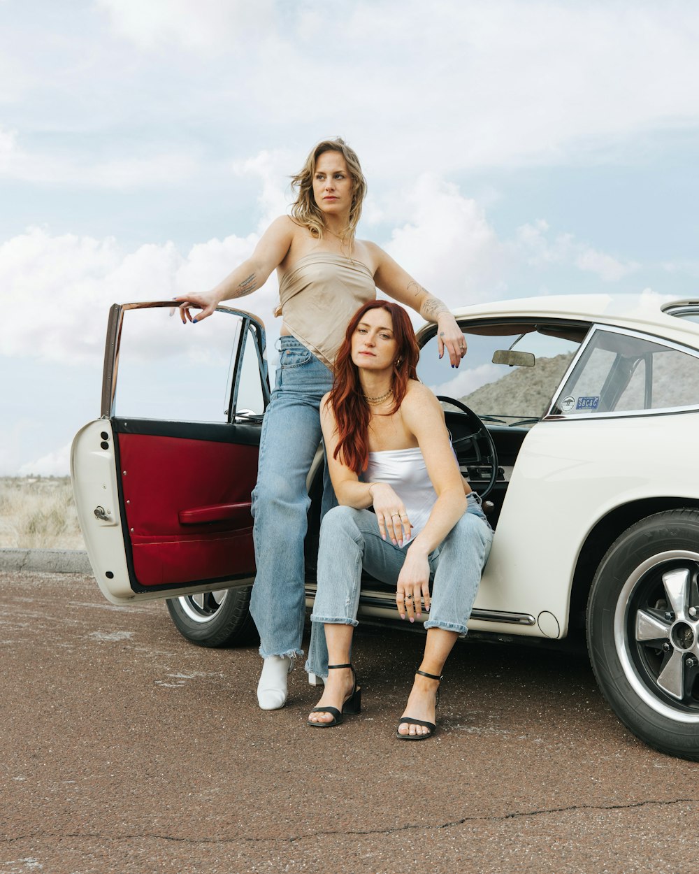 two women sitting on the hood of a car