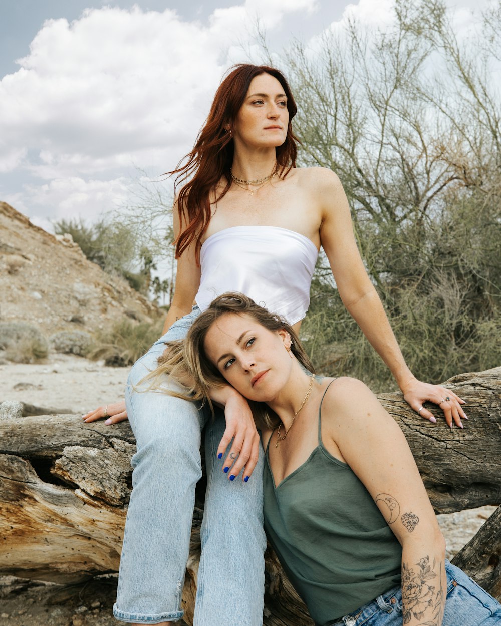 a woman sitting on a log next to another woman